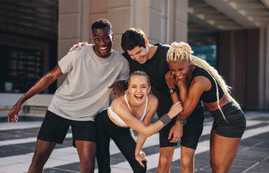 Multi-ethnic group of runners standing together after exercising session outdoors and smiling. Group of men and women in sportswear standing together and laughing after workout training. - JLPSF19589