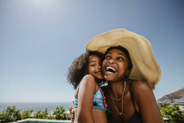 Frau mit Hut genießt den Sommerurlaub mit ihrer Tochter. Afrikanische Frau mit ihrer Tochter, die sich am Pool vergnügen. - JLPSF19614