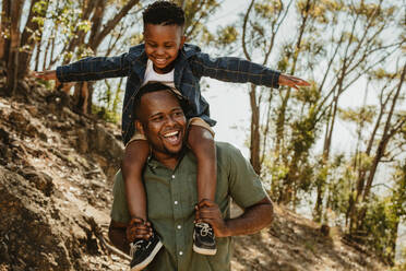 Ein Mann trägt seinen Sohn auf den Schultern, während er auf einem Bergpfad spazieren geht. Vater und Sohn haben eine tolle Zeit zusammen in ihrem Urlaub. - JLPSF19623