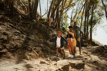 Junge Familie, die einen felsigen Bergpfad hinunterläuft. Zwei Kinder laufen mit ihren Eltern auf einem Pfad im Wald. - JLPSF19625