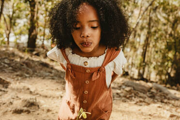 Girl blowing air on a flower in forest. Cute african girl in casuals standing in a forest. - JLPSF19629