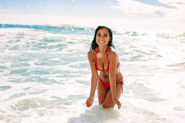 Woman in bikini standing in sea water and about to splash water. Woman on a holiday enjoying her time at the sea. - JLPSF19637