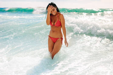 Smiling woman standing in ocean water. Woman in swimsuit having fun at the beach. - JLPSF19638