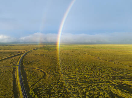 Luftaufnahme eines vollen Regenbogens über grüner Landschaft mit Ringstraße, Südisland. - AAEF16381