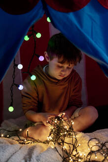Junge spielt mit beleuchteten Lichterketten im Zelt - VSNF00060