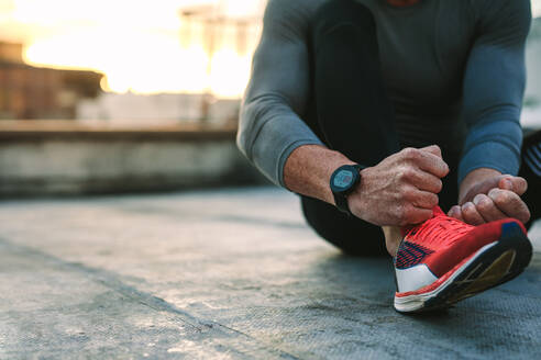 Close up of a fitness man tying lace of his sports shoes. Athlete getting ready for workout wearing shoes sitting on floor. - JLPSF19654