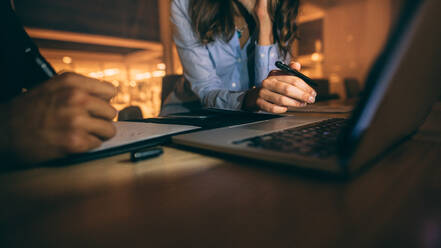 Nahaufnahme der Hände eines Geschäftsmannes und einer Frau, die sich Notizen machen und am Laptop arbeiten. Geschäftspartner sitzen spät im Büro und arbeiten am Laptop. - JLPSF19675