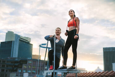 Low angle view of a fitness man and woman standing on metal stairs on terrace of a building. Fitness Paar macht eine Pause und entspannt sich auf der Terrasse eines Gebäudes. - JLPSF19677