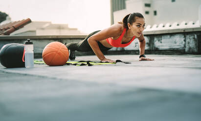 Frau Athleten tun Push-ups auf dem Dach mit Medizinball und Basketball an ihrer Seite. Frau in Fitness-Kleidung tun Workout auf der Terrasse. - JLPSF19714