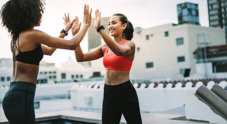 Two cheerful women in fitness wear giving high five during workout on the terrace. Women athletes doing fitness training on the rooftop giving high five. - JLPSF19723