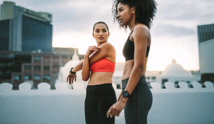 Zwei Sportlerinnen beim Workout auf dem Dach. Frauen in Fitnesskleidung beim Fitnesstraining auf einer Terrasse mit Hochhäusern im Hintergrund. - JLPSF19734