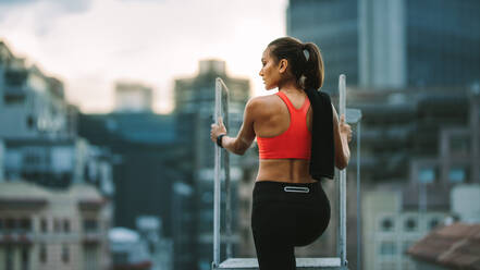 Weibliche Athletin steht auf einer Dachtreppe und schaut weg. Frau in Fitnesskleidung klettert eine Dachtreppe hinunter. - JLPSF19750