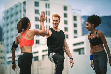 Female athlete giving high five to a man after fitness training standing on rooftop. Fitness man and women in cheerful mood giving high five. - JLPSF19763