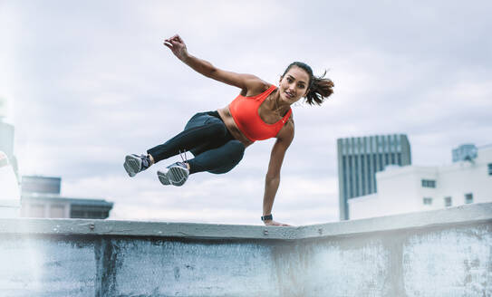 Fitness Frau springt auf die Terrasse von der Dachterrasse Zaun mit einer Hand auf Zaun. Frau in Fitness-Kleidung tun Fitness-Training auf dem Dach. - JLPSF19776