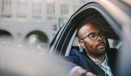 Geschäftsmann trägt Kopfhörer und hört beim Autofahren zu. Afrikanischer Geschäftsmann, der im Morgenverkehr feststeckt. - JLPSF19782