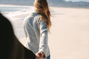 Frau hält die Hand ihres Freundes, während sie am Strand spazieren geht. Junges Paar spaziert am Strand entlang. POV des Mannes, der seiner Freundin beim Spazierengehen folgt. - JLPSF19842