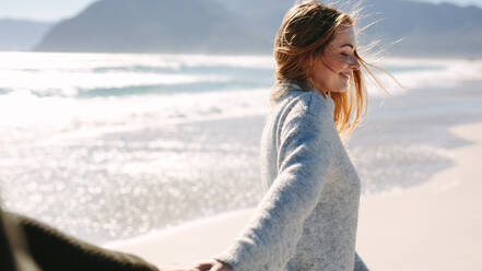 Beautiful woman enjoying walking along the beach with her boyfriend. Woman holding hands of a man while walking on the seashore. - JLPSF19845