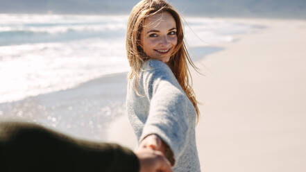 Schöne Frau, die mit ihrem Freund am Meer spazieren geht. Frau hält die Hand ihres Mannes und lächelt, während sie einen Strandspaziergang macht. - JLPSF19846
