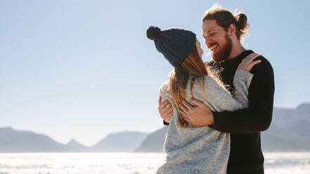 Loving couple standing at the beach embracing each other with sea in the background. Couple enjoying on a beach on a sunny day. - JLPSF19852