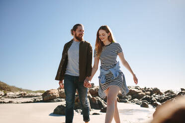Schönes Paar, das an einem felsigen Strand spazieren geht. Mann und Frau gehen Hand in Hand am Ufer entlang. - JLPSF19862