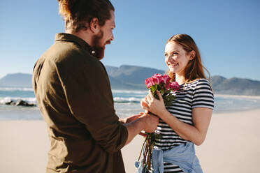 Mann gibt Überraschung Blumenstrauß von Rosen zu schönen Frau am Strand. Mann überrascht Freundin auf ein romantisches Datum. Paar in der Liebe am Strand. - JLPSF19883
