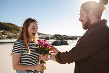 Freund überrascht Freundin mit Blumen am Strand. Mann überrascht Frau mit Rosenstrauß bei einem romantischen Date. - JLPSF19885