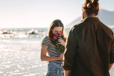 Schöne Frau riecht Blumen am Strand mit Freund. Frau liebt die Überraschung von ihrem Freund gegeben. Loving Paar am Strand. - JLPSF19888