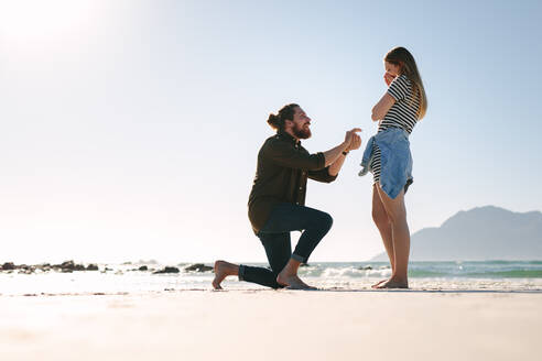 Mann kniet vor Frau und macht ihr einen Heiratsantrag. Mann macht Frau am Strand einen Heiratsantrag. - JLPSF19889