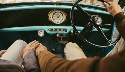 Nahaufnahme eines älteren Paares, das sich beim Autofahren an den Händen hält. Der alte Mann fährt das Auto und die Frau sitzt auf dem Beifahrersitz und hält seine Hand. - JLPSF19904