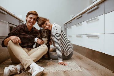Lächelnder Mann und Frau, die mit ihrem Hund zu Hause auf dem Boden sitzen. Porträt einer glücklichen, hundeliebenden Familie mit ihrem Hund. - JLPSF19917
