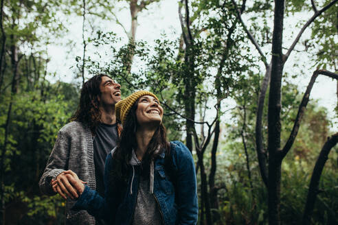 Young man and woman in forest looking up and smiling. Beautiful couple spending time together in forest. - JLPSF19922