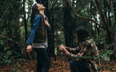 Young man kneeling with a ring and making marriage proposal to beautiful girl at forest. Young guy proposing a cheerful girl outdoors in park. - JLPSF19928