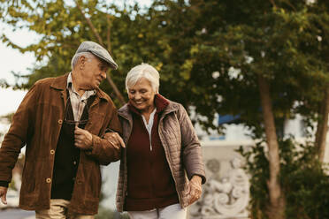 Porträt eines älteren Paares, das sich unterhält und an einem Wintertag im Freien spazieren geht. Älterer Mann hält die Hand seiner Partnerin und geht auf der Straße. - JLPSF19934