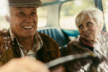 Lächelnder älterer Mann, der ein Auto mit einer Frau auf dem Beifahrersitz fährt. Glückliches altes Paar, das mit dem Auto unterwegs ist. - JLPSF19937