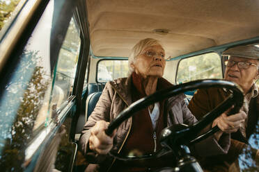 Alte Frau fährt Auto und unterhält sich mit ihrem Mann auf dem Beifahrersitz. Älteres Paar fährt in einem Oldtimer. - JLPSF19945