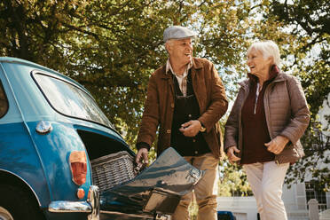 Ein alter Mann und eine Frau packen einen Picknickkorb in ihren Kofferraum. Ein älteres Paar macht ein Picknick an einem Wintertag. - JLPSF19956