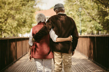 Rückansicht eines älteren Paares, das gemeinsam durch einen Park spaziert. Alter Mann und Frau in warmer Kleidung gehen gemeinsam durch einen Park. - JLPSF19965