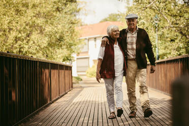 Fill length of happy elderly couple walking through a park. Senior man and woman walking together in park in a winter day. - JLPSF19966