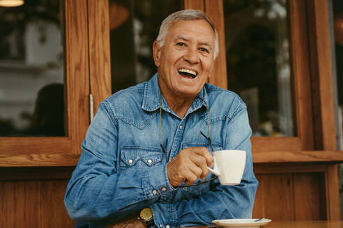 Porträt eines fröhlichen älteren Mannes, der in einem Café Kaffee trinkt. Lächelnder alter Mann, der sich im Café entspannt. - JLPSF19973