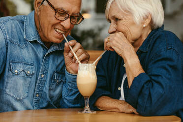 Nahaufnahme eines verliebten, glücklichen älteren Paares in einem Café, das kalten Kaffee aus demselben Glas trinkt. Alter Mann und Frau genießen einen kalten Kaffee auf dem Tisch. - JLPSF19976