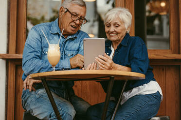 Glückliches Paar im Ruhestand sitzt in einem Café und benutzt ein digitales Tablet. Alter Mann und Frau benutzen einen Tablet-PC in einem Café. - JLPSF19978