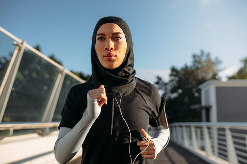 Gesunde, sportliche Frau mit Hijab beim Joggen im Freien in der Stadt. Islamische Frau beim Laufen am frühen Morgen. - JLPSF19987