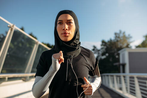 Healthy sporty woman wearing hijab jogging outdoors in the city. Islamic woman running early in the morning. - JLPSF19987