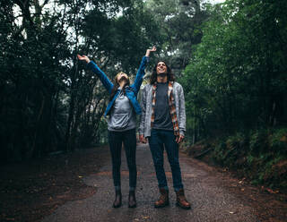 Junges Paar auf einem Spaziergang im Wald während des Regens, das sich amüsiert. Junger Mann und Frau stehen auf einem Pfad im Wald und genießen den Regen. - JLPSF20046