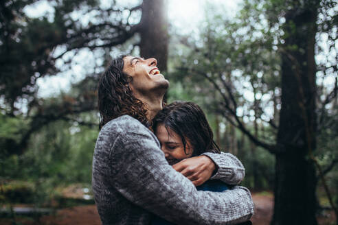 Verliebtes Paar umarmt sich im Park bei Regen. Lächelnder junger Mann umarmt seine Freundin bei Regen. - JLPSF20054