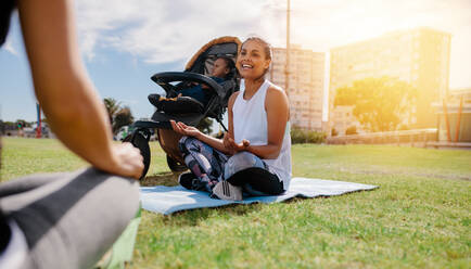 Active mothers doing yoga in park with baby in a stroller. Woman sitting in park in the morning practicing yoga with baby in a pram. - JLPSF20063