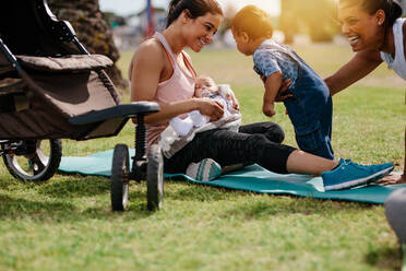 Smiling mothers sitting in park with their babies after the morning walk. Active moms with their kids spending time in park early in the morning. - JLPSF20064