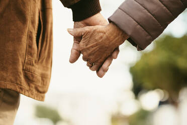 Close up of senior man and woman holding hands and walking outdoors. Rear view of old couple walking hand in hand outdoors. - JLPSF20093