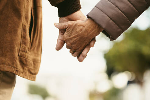 Nahaufnahme eines älteren Mannes und einer Frau, die sich an den Händen halten und im Freien spazieren gehen. Rückansicht eines alten Paares, das Hand in Hand im Freien spazieren geht. - JLPSF20093