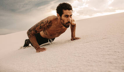 Fit Mann macht Push-ups über Sanddünen. Muskulöser Mann trainiert auf Wüstensand. - JLPSF20113